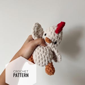 May include: A crocheted chick toy with a red comb, brown legs, and white body. The toy is being held in a hand. The text "CROCHET PATTERN" is visible in the image.