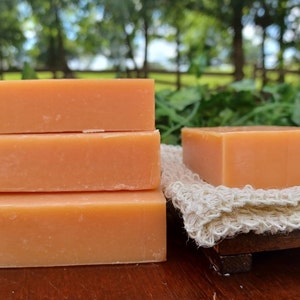 May include: Three bars of orange soap stacked on top of each other. The soap is on a wooden surface.