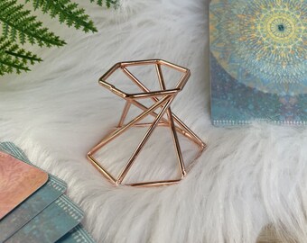 Könnte beinhalten: Ein geometrischer Kristallständer aus Roségold mit sechseckiger Basis und pyramidenförmigem Oberteil. Der Ständer besteht aus dünnem Metalldraht und eignet sich perfekt zum Ausstellen von Kristallen oder anderen kleinen Gegenständen.