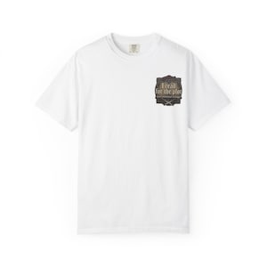 Könnte beinhalten: Ein weißes Kurzarm-T-Shirt mit einer kleinen Grafik auf der linken Brust. Das Design ist eine dunkle, verzierte Schildform, die den Text "I read for the plot" in einer Serifenschrift enthält, mit zwei gekreuzten Schwertern unter dem Text.