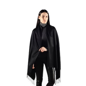 May include: A black pashmina scarf with fringe. The scarf is draped around a person's neck and shoulders.