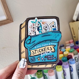 Könnte beinhalten: Ein Sticker-Paket mit einer Cartoon-Illustration einer Sardinen-Dose mit dem Text "7 lil' fishes & lemon STICKERS PACK". Die Dose ist gelb mit einem blauen Deckel und enthält drei Cartoon-Fische.