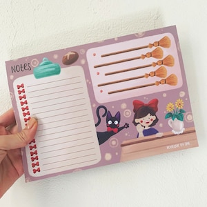 Peut inclure: Un planificateur rose et violet avec un chat noir, une fille avec un nœud rouge et un balai. Le planificateur a une section pour les notes et une section pour une liste de choses à faire. Le texte "Notes" est en haut du planificateur. Le texte "Boutique by Shi" est en bas du planificateur.