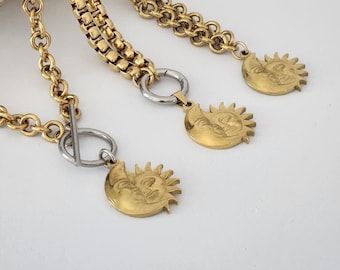 May include: Three gold chain necklaces with sun and moon pendants. The chains are different styles, one is a box chain, one is a curb chain, and one is a cable chain. The pendants are all the same design, a sun and moon with a face.