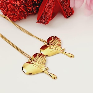 May include: Two gold heart-shaped necklaces with a dripping design. The necklaces are on a white surface.