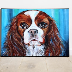 Op de afbeelding: Een schilderij van een Cavalier King Charles Spaniel hond met bruin en wit haar. De hond kijkt rechtstreeks naar de kijker met een serieuze uitdrukking. De achtergrond is een blauw en groen abstract ontwerp.