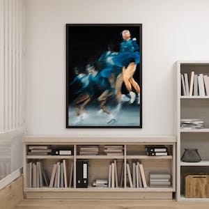 May include: A framed art print showing a blurred image of a dancer in a blue outfit. The artwork is set against a dark background, with the dancer's form captured in a series of overlapping movements. The print is displayed above a wooden bookshelf filled with books and files.
