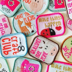 Könnte beinhalten: Sortiment an bunten Bügelbildern mit verschiedenen Designs und Sprüchen, darunter "What the Fuchs", "Make things happen", "Bullshit Free Zone" und "Craft Club".