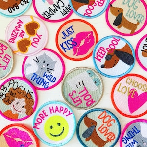 Könnte beinhalten: Eine Sammlung bunter gestickter Bügelbilder mit verschiedenen Sprüchen und Designs, darunter "You Are Amazing", "Just Kiss", "Keep Cool", "Dog Lover", "Wild Thing", "More Happy", "Focus on the Good" und "Choose Love".