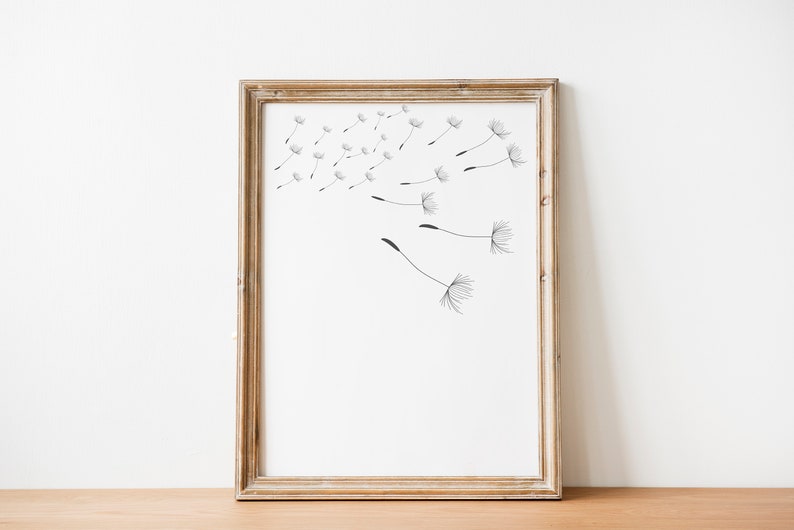 May include: A framed print of a black and white illustration of dandelion seeds blowing in the wind. The frame is a light brown wood.