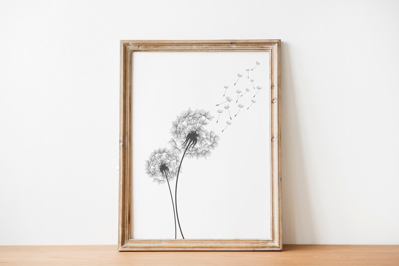 May include: A framed black and white print of two dandelion flowers with seeds blowing in the wind. The print is in a light wood frame.