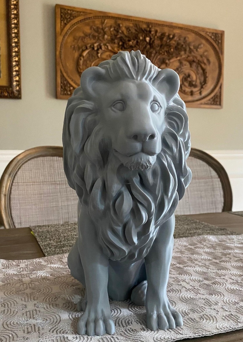 May include: A gray lion statue with a detailed mane and facial features. The sculpture is seated on a table with a patterned runner. Decorative wall art is visible in the background.