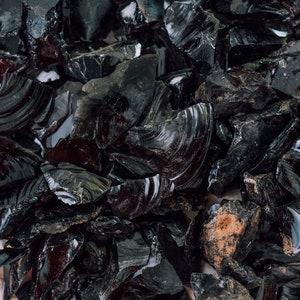 May include: A close-up of a pile of black obsidian shards. The shards are sharp and have a glassy sheen.