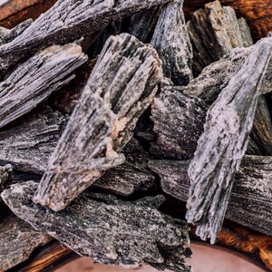 May include: A close-up of a pile of black, rough, and textured crystals. The crystals are in a wooden bowl.