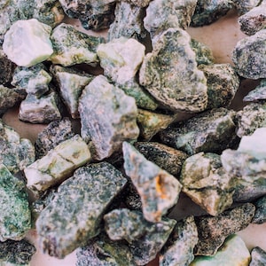 May include: A close-up of a collection of small, green, and gray stones. The stones are irregularly shaped and have a rough texture.