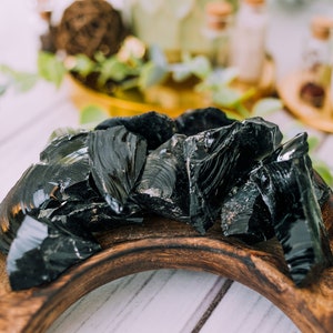 Puede incluir: Una colecci&oacute;n de piedras de obsidiana negra en un cuenco de madera. Las piedras son lisas y brillantes, y tienen un color oscuro, casi negro.