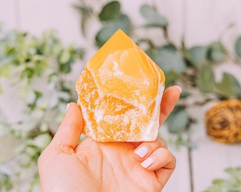May include: A large, yellow, natural crystal in the shape of a point, held in a hand. The crystal has a rough, textured surface.