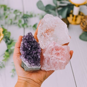 May include: Three raw crystals: a purple amethyst cluster, a clear quartz cluster, and a pink rose quartz cluster.