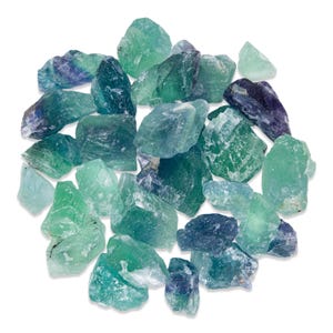 May include: A collection of raw fluorite crystals in shades of green, blue, and purple. The natural, rough-cut stones vary in size and shape, with a translucent quality. The crystals are scattered against a white background.