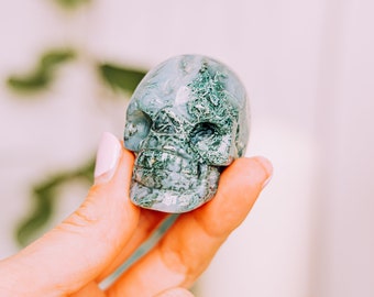 May include: Green moss agate skull carving. The skull is detailed with intricate patterns and textures.