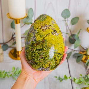 May include: A polished, egg-shaped stone featuring a vibrant mix of lime green, olive, and dark forest green hues with intricate black veining and small crystalline inclusions throughout the smooth, glossy surface of the mineral specimen.