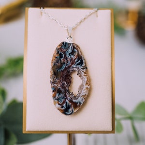 May include: A silver chain necklace with a pendant made from a slice of agate. The agate is brown, white, and blue with a natural hole in the center.