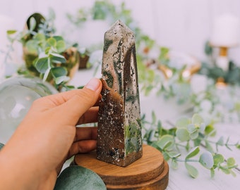 May include: A gold pyrite crystal point on a wooden base. The crystal is a dark gold color and has a rough, textured surface. The base is a dark brown color and has a smooth, polished surface.