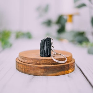 May include: Black tourmaline crystal keychain on a wooden stand. The crystal is attached to a silver key ring.