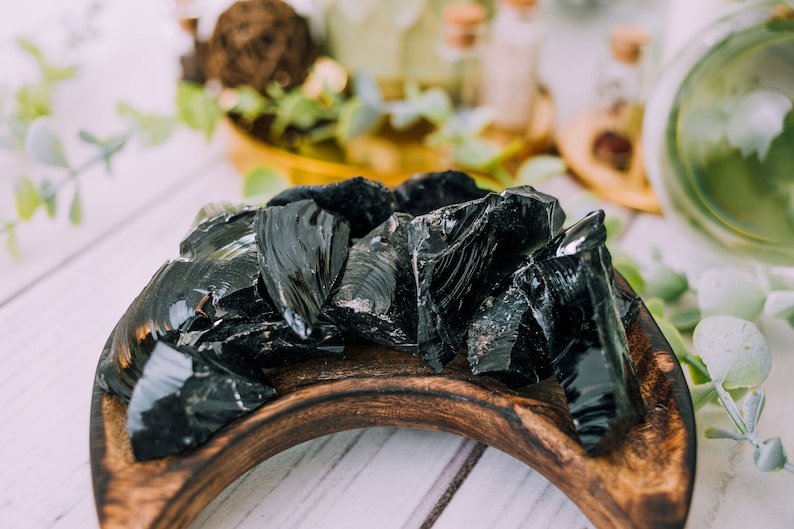 Puede incluir: Una colecci&oacute;n de piedras de obsidiana negra en un cuenco de madera. Las piedras son lisas y brillantes, y tienen un color oscuro, casi negro.