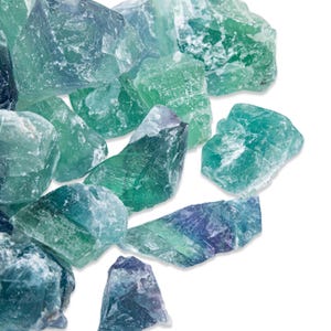 May include: A collection of raw fluorite crystals in shades of green, blue, and purple. The natural stones have a rough, textured surface and varying shapes. The crystals are arranged on a white background, showcasing their natural beauty.