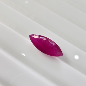 May include: A marquise-cut gemstone with a vibrant, deep magenta-pink hue. The stone features a faceted surface that reflects light, creating a brilliant appearance. The elongated, pointed shape is characteristic of a marquise cut, showcasing clarity.