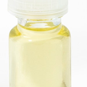 May include: A small, clear glass bottle with a white cap, filled with a light yellow liquid. The bottle is cylindrical with a rounded base. The cap is a solid, opaque white. The background is plain white.