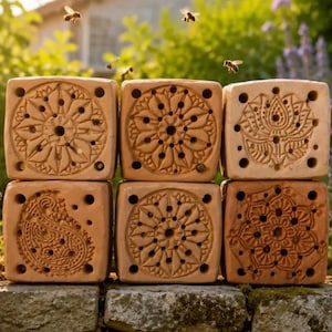 Könnte beinhalten: Ein Stapel aus sechs quadratischen Bienenhäusern aus Terrakotta mit aufwendig geschnitzten Mustern auf den Vorderseiten, darunter Blumen-, Mandala- und Paisley-Designs mit mehreren kleinen kreisförmigen Löchern zum Nisten.
