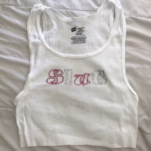 May include: White ribbed tank top with the word "BLITZ" spelled out in pink and silver rhinestones.