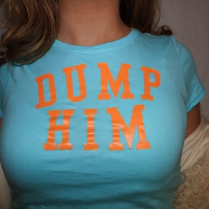 Könnte beinhalten: Ein türkisfarbenes T-Shirt mit dem Aufdruck "DUMP HIM" in Orange.