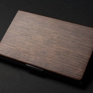 May include: A dark brown wooden business card holder with a black metal trim. The holder is made of a natural wood grain.