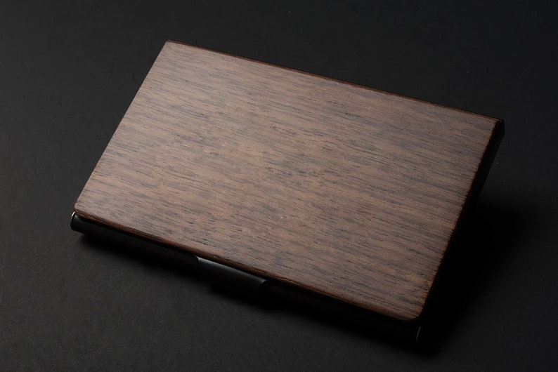 May include: A dark brown wooden business card holder with a black metal trim. The holder is made of a natural wood grain.