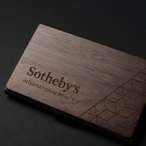May include: A dark brown wooden business card holder with a geometric pattern and the text "Sotheby's International Realty" engraved on the front.