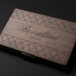 May include: A wooden business card holder with a diamond pattern and the text "Berrettini EST 2021" engraved on the front.