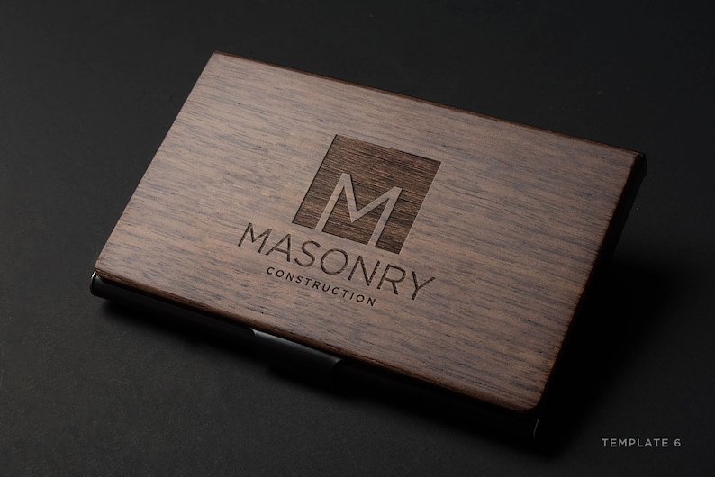May include: A wooden business card holder with a black metal clip. The holder has a laser-engraved logo with the letter "M" inside a square and the text "MASONRY CONSTRUCTION".
