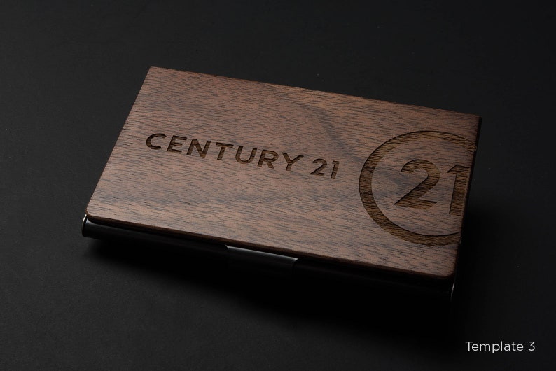May include: A wooden business card holder with a black metal trim. The holder has the text "CENTURY 21" and a circle with the number "21" engraved on the front.