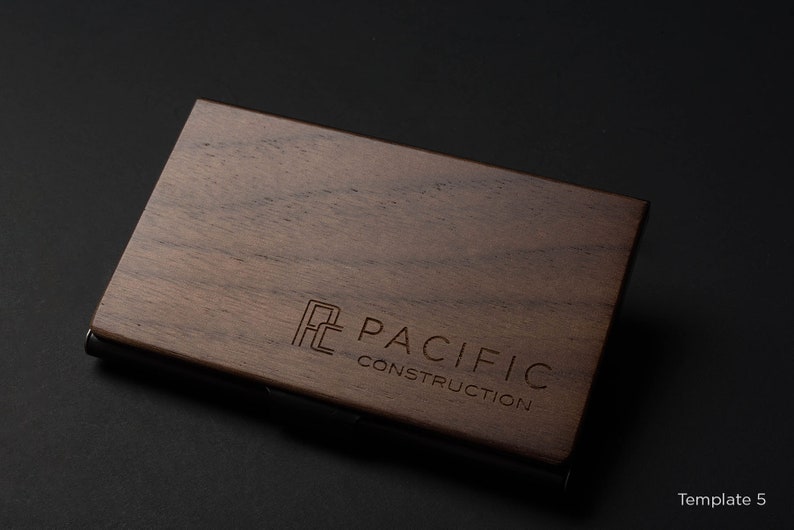 May include: A wooden business card holder with a metal edge. The holder has the logo "PC PACIFIC CONSTRUCTION" engraved on the front.