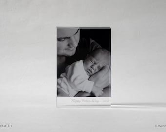 May include: A black and white photo of a baby being held by an adult, printed on a clear acrylic block. The text "Happy Fathers Day - 2020" is printed on the bottom of the block. The image is a portrait.