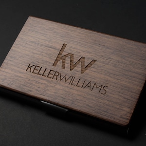 May include: A wooden business card holder with a black metal edge. The holder is engraved with the Keller Williams logo and the text "Keller Williams".