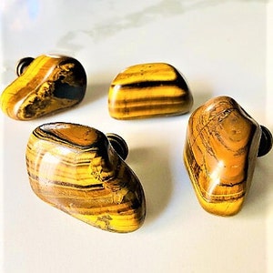 May include: Four tiger's eye stone cabinet knobs with a gold finish. The knobs are irregularly shaped and have a natural, polished look.