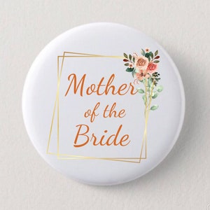 May include: A white button with a gold frame and floral design. The text "Mother of the Bride" is written in orange.