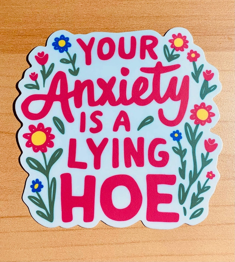 May include: A sticker with the text "YOUR Anxiety IS A LYING HOE" in red, surrounded by floral illustrations. The background is light blue, and the flowers are red, yellow, and blue.