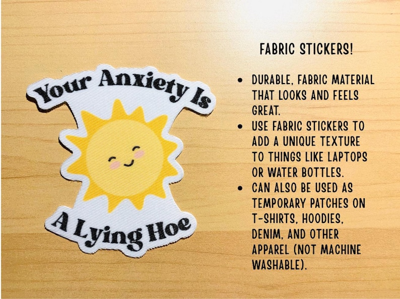 May include: A fabric sticker with the text "Your Anxiety Is A Lying Hoe" and a smiling sun graphic. The sticker is white with black text and a yellow sun. It can be used on laptops, water bottles, or apparel.