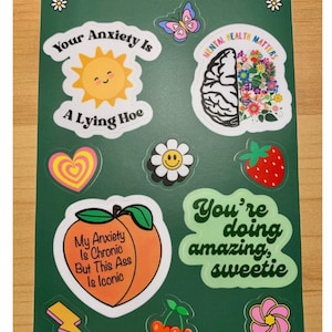 May include: A sheet of stickers with various designs and text. Designs include a smiling sun, a brain with flowers, a peach with text, and a daisy. Text includes "Your Anxiety Is A Lying Hoe" and "Mental Health Matters".