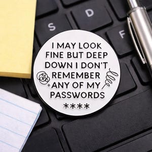May include: A white and black round coin with the text "I MAY LOOK FINE BUT DEEP DOWN I DON'T REMEMBER ANY OF MY PASSWORDS" on a black keyboard. A yellow sticky note and a pen are also visible.